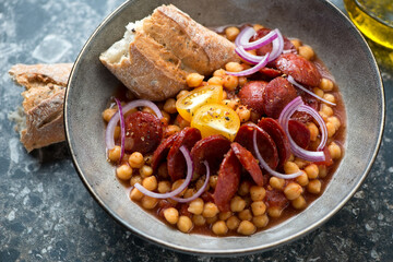 Stew with chorizo, chickpeas and red onion served in a grey bowl, middle close-up, selective focus, studio shot