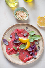 Plate with carpaccio made of raw marbled beef, vertical shot on a beige marble background, high angle view
