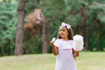 Funny girl in pink dress eats cotton candy in summer in the park