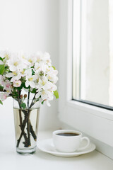 Spring flowers in a vase and a cup of tea or coffee in a white porcelain mug on the windowsill