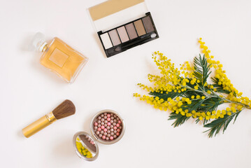 Makeup cosmetics, hydrogel patches, toilet water, makeup brushes and a branch of yellow mimosa on a light background. Flat lay fashion blogger