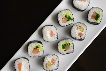 Rolls with cheese and salmon on a white rectangular plate on a dark background.