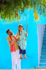 Indian farmer swinging to her daughter at home.