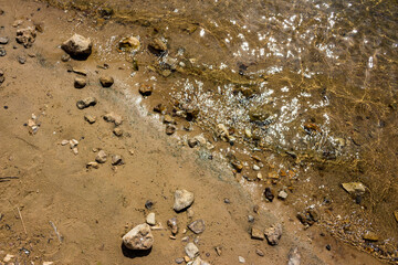 Texture of the sandy shore with stones and water shining in the sun