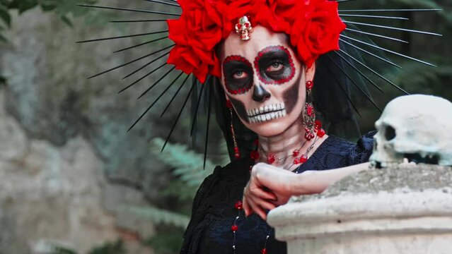 A woman with a design on her face in the style of the Goddess of Death with a sugar skull next to her stares straight ahead. Festival Day of the Dead