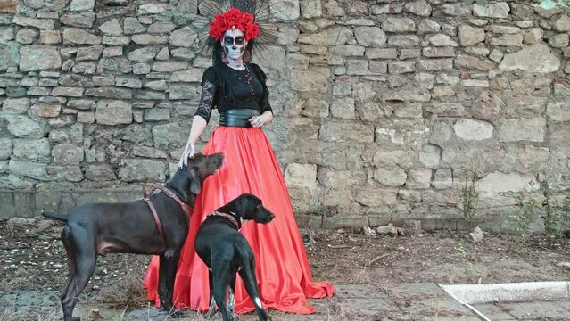 A young Woman with a design on her face in the style of the Goddess of Death with two magnificent dogs. Kindness and tenderness of the ancient holiday Day of the Dead