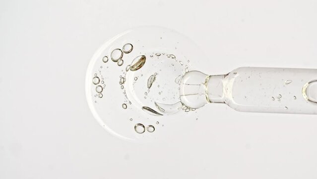 Transparent cosmetic gel fluid, serum with molecule bubbles oil in pipette drips on a white background. Macro Shot of Natural Organic Cosmetics, Medicine. Production Close-up. Slow Motion. 4k
