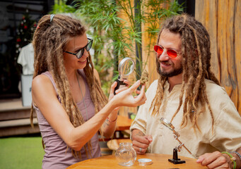 Hippie style couple examines under a magnifying glass the joints and buds of medical marijuana