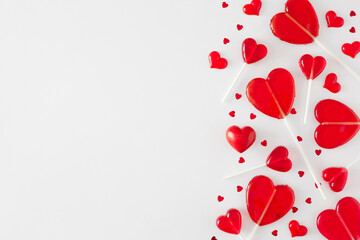 Valentines Day celebration concept. Flat lay photo of red heart shaped lollipops and sprinkles on white background with copy space. Love Valentines card idea.