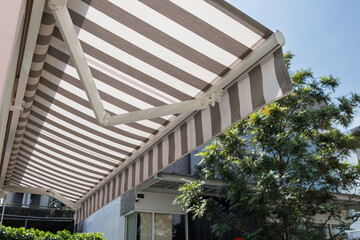 white and grey striped awning of shop with house and tree background. exterior canvas roof shading...