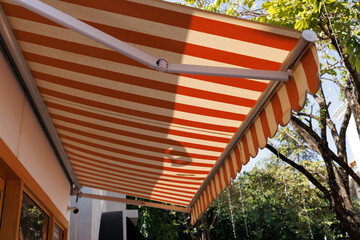 white and orange striped awning of shop with house and tree background. exterior canvas roof shading for sun protection. - obrazy, fototapety, plakaty