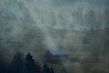 Misty autumn countryside landscape with a ray of light. Small hut and haystack