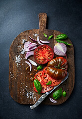 Freshly chopped tomatoes, red onion, basil and sea salt on a wooden chopping board. Top view - 557687383