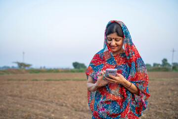 Indian rural woman in traditional saree and using smartphone at agriculture field.