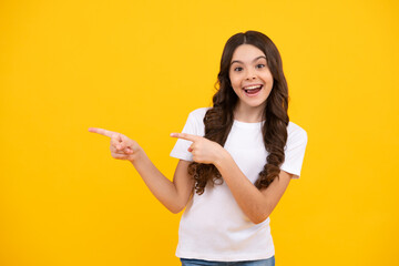 Amazed teenager. Positive teenager child points aside with cheerful expression, shows amazing at blank empty space. Advertisement and mockup. Excited teen girl.
