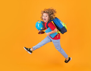 Fototapeta na wymiar Shool kid jump with school bag and globe. Full length body of little school kid jumping having fun isolated yellow color background. Crazy school boy jump.