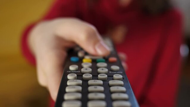 Close-up of the TV remote control in the hands of a child who switches TV channels. The child girl picks up the TV remote and presses the buttons.