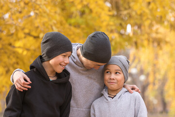 Three brothers hugging. Smiling boys of different ages outdoor in autumn, close up, selective focus.