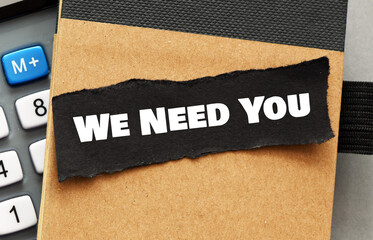 WE NEED YOU words on a small black piece of paper.