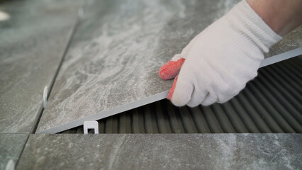 Workers are laying the floor with large tiles. A worker puts a large tile on the floor. Workers are installing a large ceramic tile on the floor.