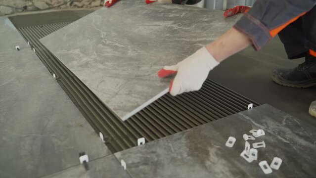 Workers are laying the floor with large tiles. A worker puts a large tile on the floor. Workers are installing a large ceramic tile on the floor.