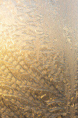 Evening sun and bright blue sky through the frost pattern on the window. Ice pattern and sunlight on winter glass