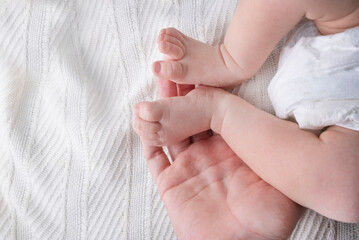 Female hands hold the baby's legs on a light or white background close-up