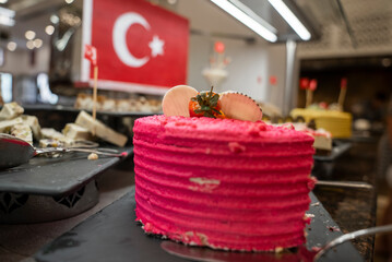 Close-up of half-eaten cake with pink whipped cream served on table with Turkish flag in the background at buffet in restaurant