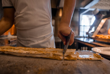 Midsection of male chef cutting Turkish cheese pide into slices with cutter on table in commercial kitchen at restaurant