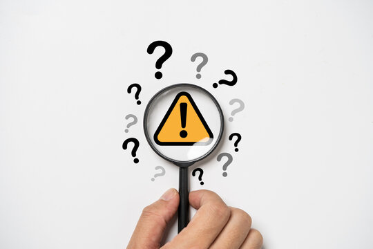 Hand holding magnifier glass with yellow triangle caution warning sign and question mark for notification error and maintenance concept.