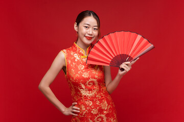 Young asian woman wearing qipao cheongsam dress with Chinese folding fan on red background for...
