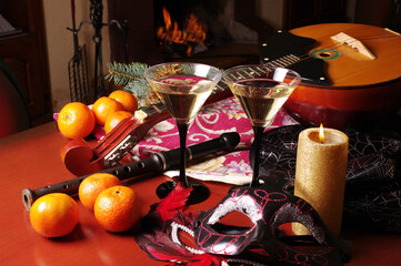 Two glasses of wine, domra, flute, burning candle, carnival masks, tangerines, Christmas decorations on the background of the fireplace.