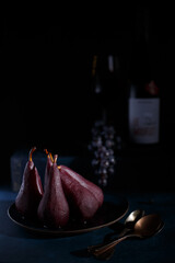 Poached pears in red wine on a blue plate and wood background. Grapes and bottle of wine in the...