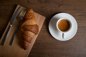 Croissant with espresso in white cup on wooden background
