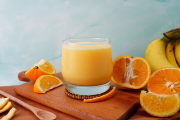 Orange fruit smoothie in a glass with fresh orange slices on wooden background