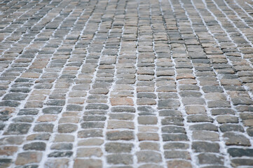 The vintage road is paved with old cobblestones. Paving stones with snow close-up. Winter...