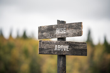 vintage and rustic wooden signpost with the weathered text quote rise above, outdoors in nature. blurred out forest fall colors in the background.