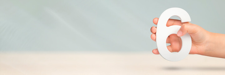 Number six in hand. Hand holding white number 6 on blurred background with copy space. Concept with...