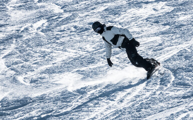 Snowboarder coming down the slope with bright backlight carving snow on the edge of the board in high speed