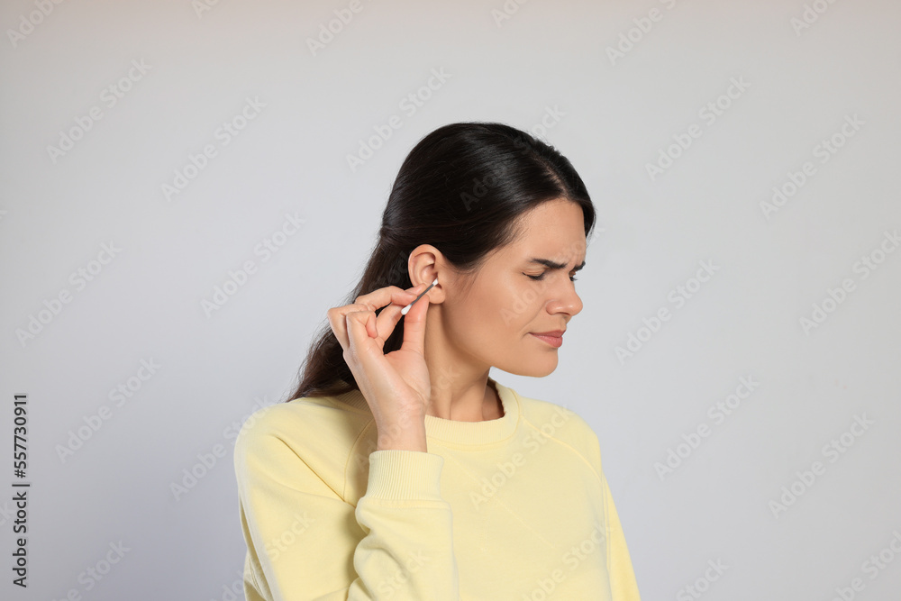 Sticker Young woman cleaning ear with cotton swab on light grey background