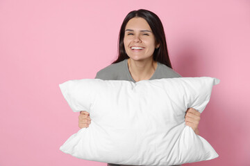 Happy young woman with soft pillow on pink background