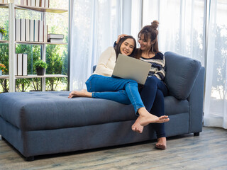Beautiful young Asian women LGBT lesbian couple happy couple sitting on the sofa in the living room, using the laptop computer bought online at home. LGBT lesbian couple together indoors concept