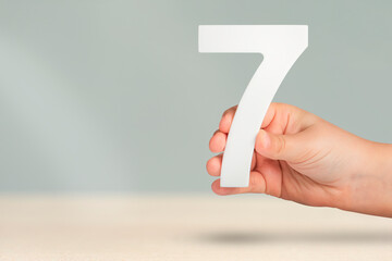 Number seven in hand. Hand holding white number 7 on blurred background with copy space. Concept...