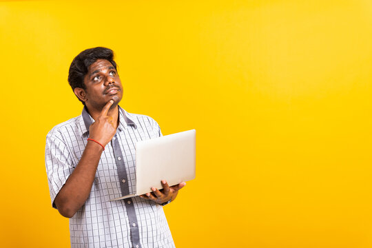 Closeup Asian happy portrait young black man holds a laptop computer hand finger handle on the chin and thinking question looking away, studio isolated on yellow background