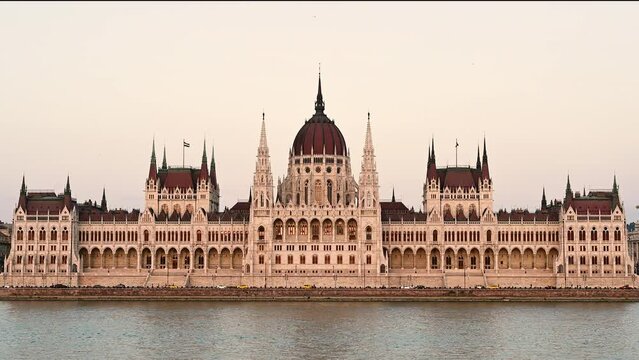 Budapest, Hungary, August 2022. Stunning footage of the parliament seen frontally from the Danube river side. The yellow light of late afternoon warms the facade.