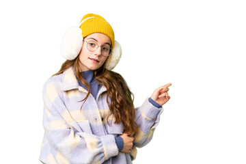 Teenager girl wearing winter muffs over isolated chroma key background pointing finger to the side