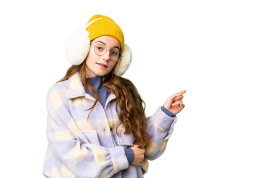 Teenager girl wearing winter muffs over isolated chroma key background pointing finger to the side