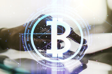 Double exposure of creative Bitcoin symbol hologram and hand working with a digital tablet on background. Mining and blockchain concept