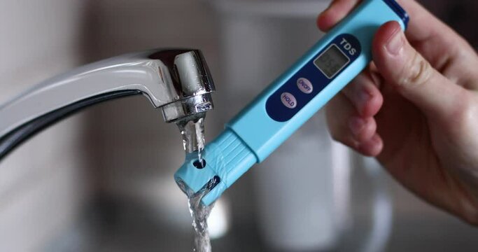 A person brings a tds meter to the tap with running water and checks its quality. The concept of using clean water