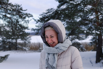 Obraz premium Portrait of happy beautiful elderly senior retired woman in age is playing, having fun with snow outdoors in forest or park at winter cold day, smiling, enjoy weather